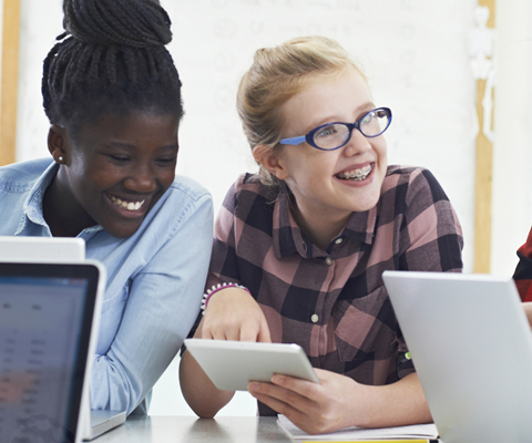 students collaborating at a table, using laptops and tablets