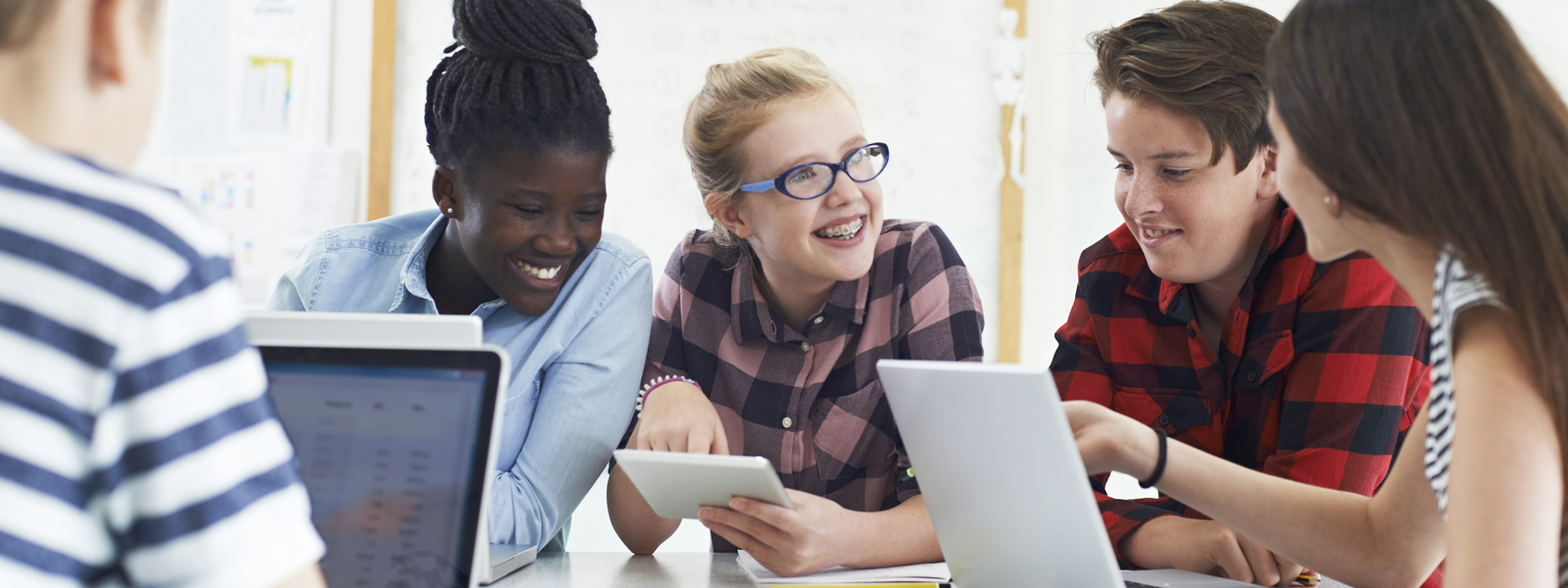 students collaborating at a table, using laptops and tablets