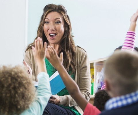 teacher lecturing with enthusiastic students raising hands