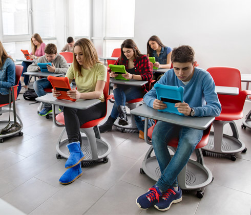 students reading at their desks, using tablets
