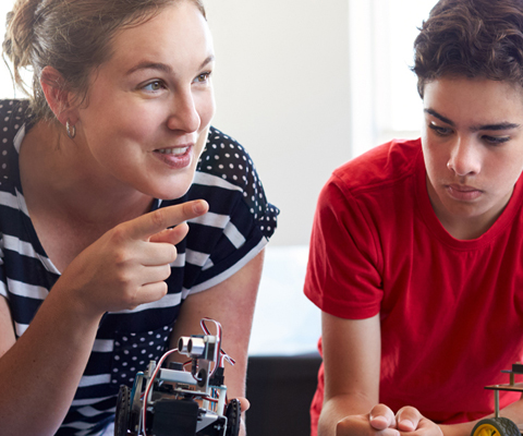 teacher leaning in to help students with robotics