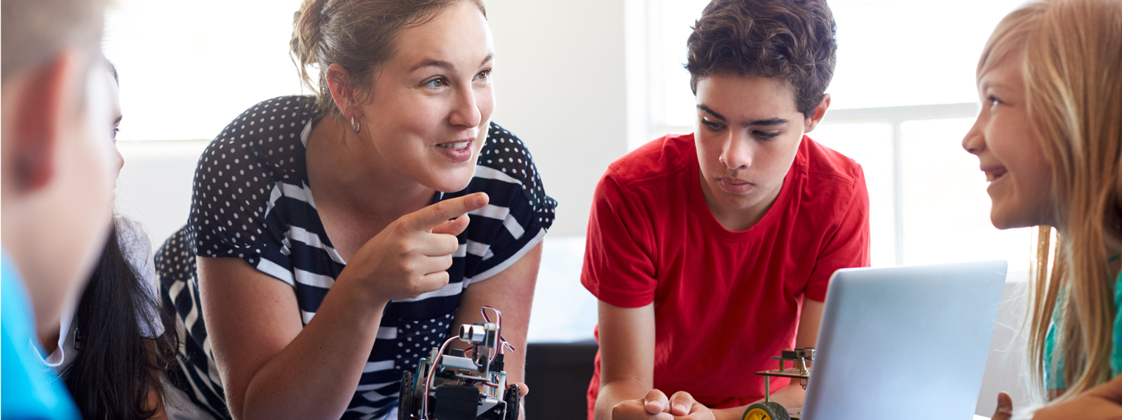teacher leaning in to help students with robotics